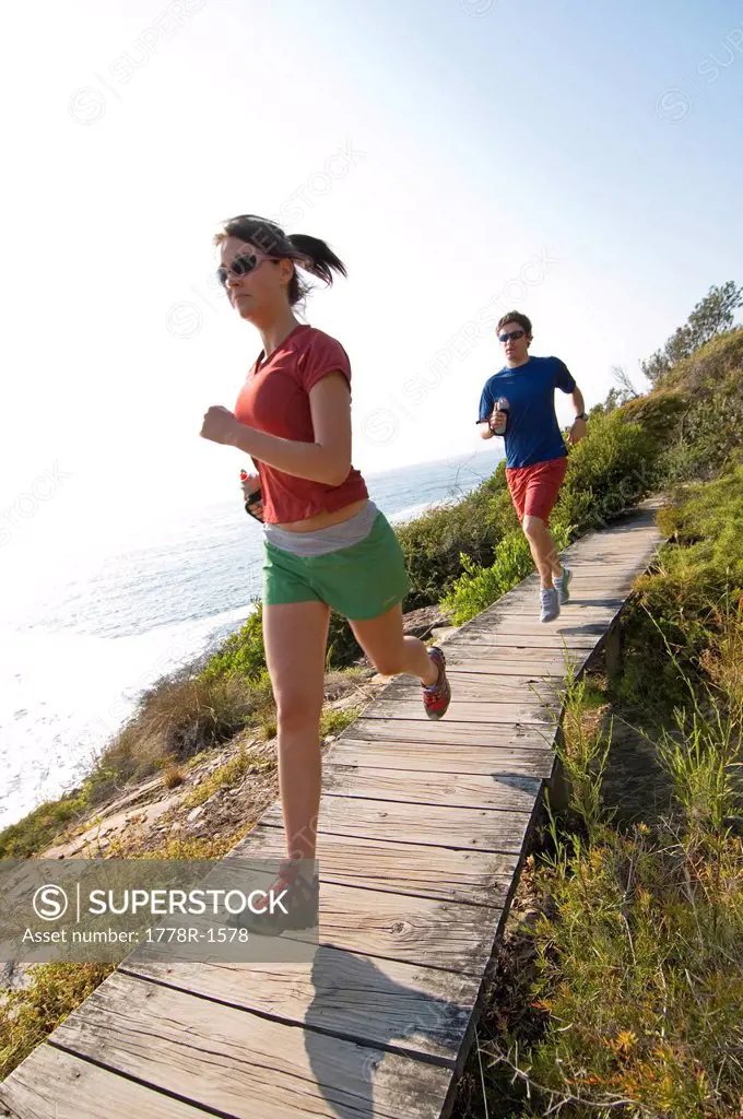 Runners on bridge along ocean trail.