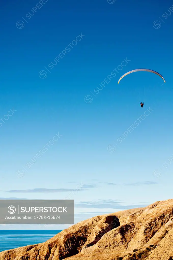 On a bright blue sky a hang glider flies above the cliffs in Torrey Pines in La Jolla, California.