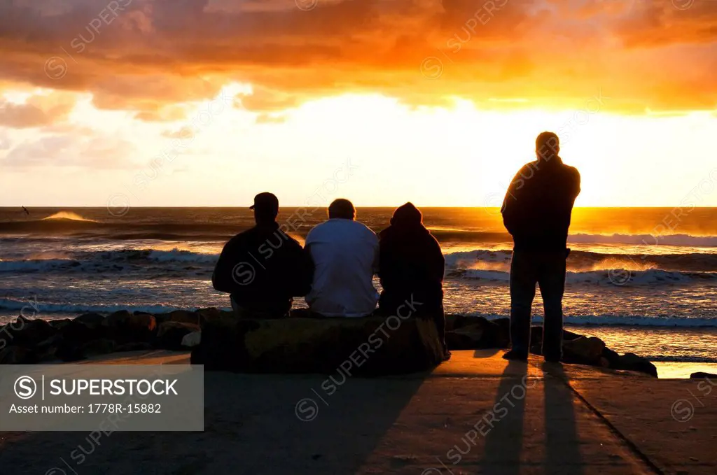 Four men watching the sunset on the ocean on a stormy day in San Diego, California.