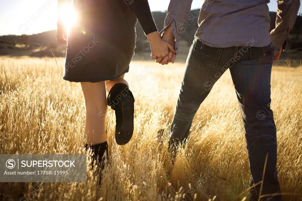 Low shot of couple´s body holding hands and walking away in an open field.