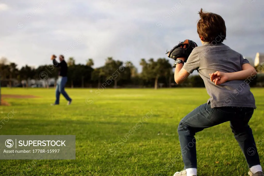 A kid wearing a baseball glove waits for his dad to throw the ball at the park.