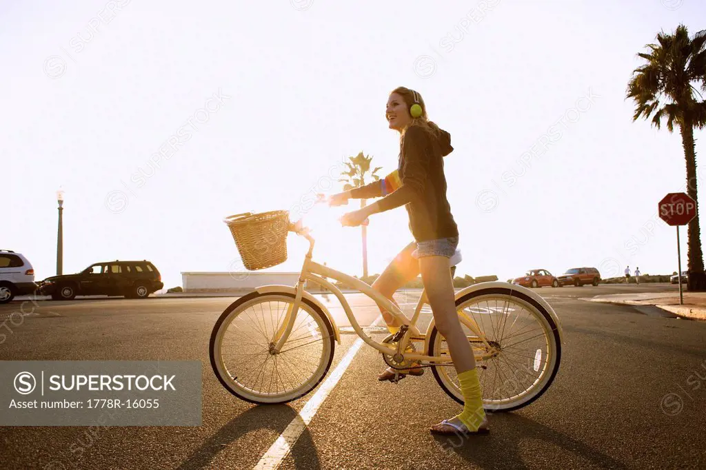 Young woman wearing a headphone, yellow socks and a hoodie rides a cruiser bike to the beach.