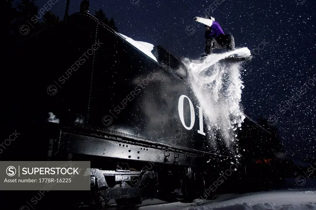 A male young adult jumps off a train at night in Colorado.