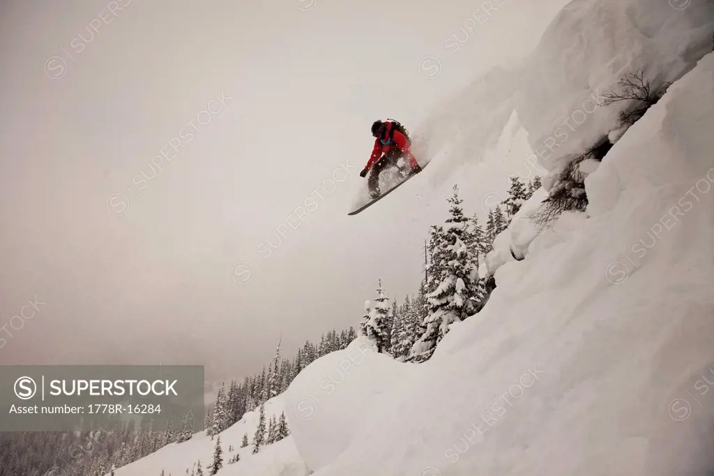 A snowboarder jumps off a cliff into powder in Colorado.
