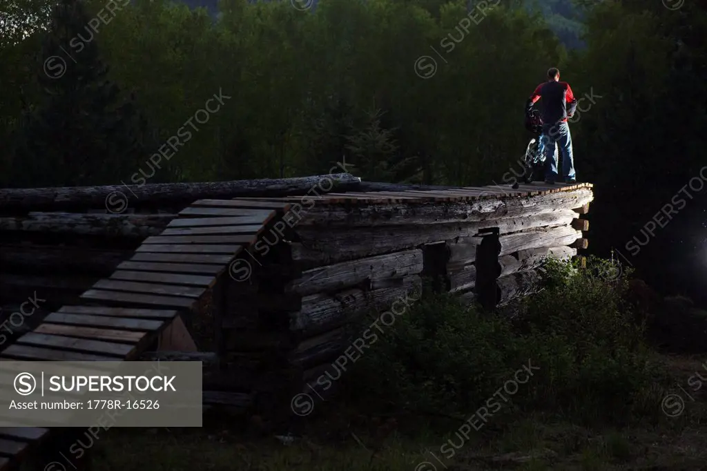 A mountain biker stands on top of a log cabin feature thinking about the drop in Idaho.