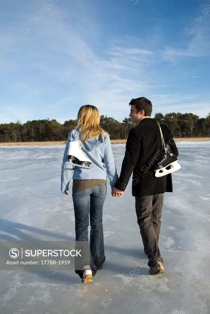 Young couple walking with skates on frozen pond.