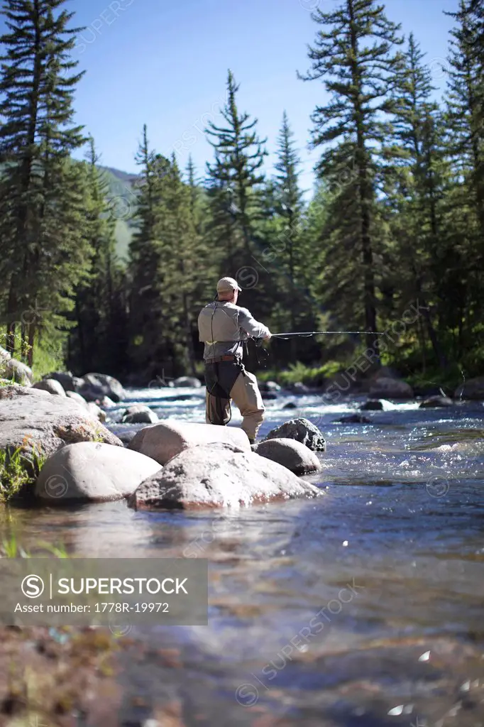 Fisherman standing by the rocks goes fly fishing at a river in Vail.