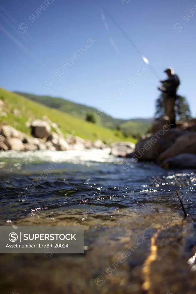 Shot of water running in the river with blurred background of a fisherman standing on the rocks.