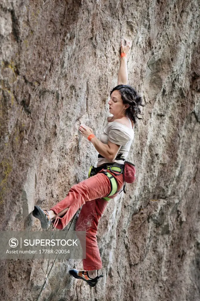 A middle aged woman wearing white tshirt and red pants rock climbing in Jilotepec, Estado de Mexico, Mexico.