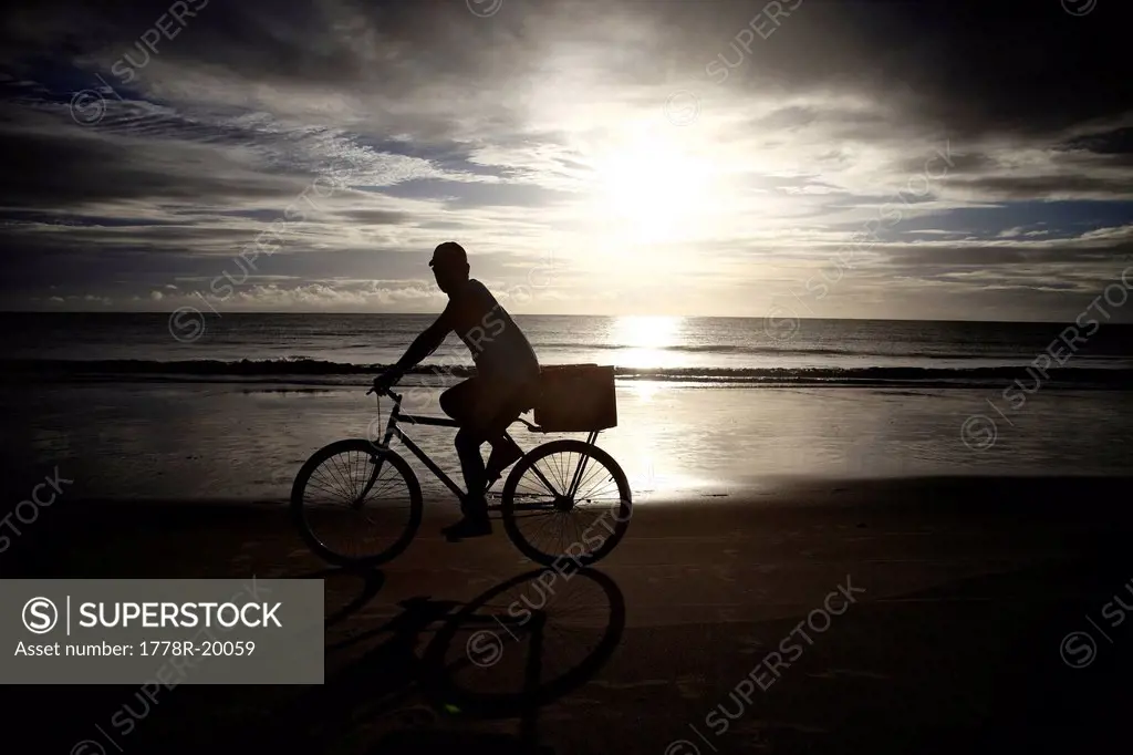 A male rides his bike to work at the beach at sunrise.