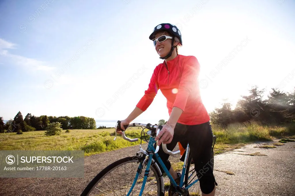A young woman smiles as she stands next to her bike as the sun sets over her shoulder.