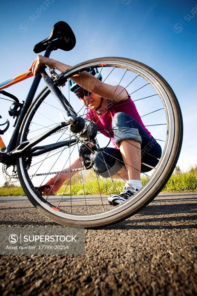 A young woman inspects her chain and back tire on the way home from work on her commuting bike.