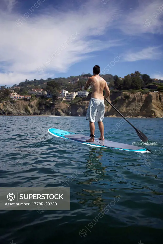 Male stand up paddling away from the camera.