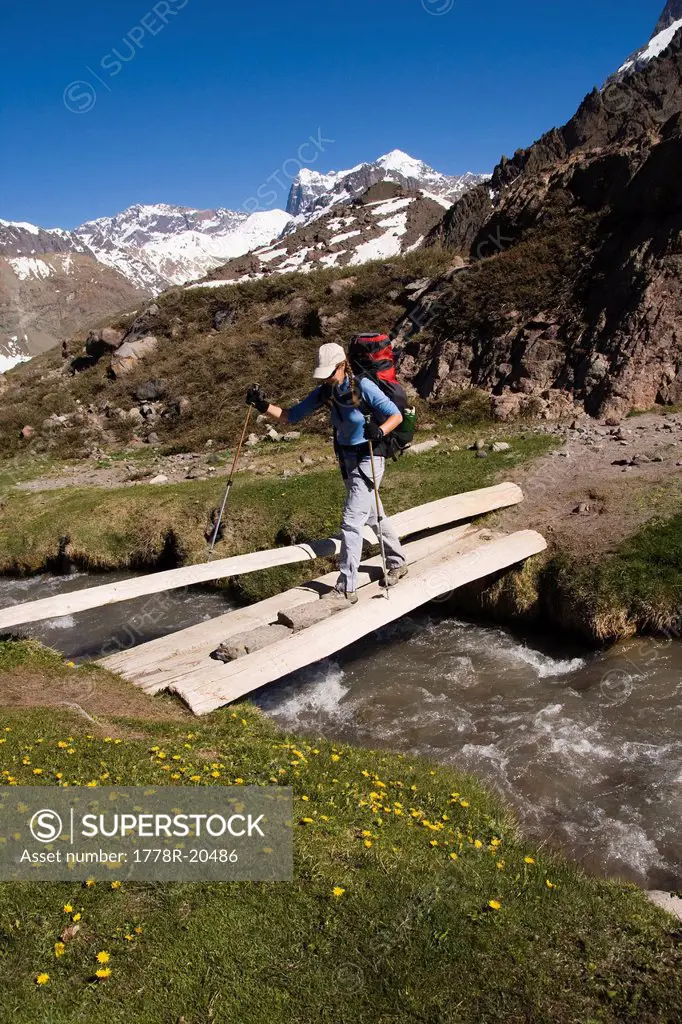 A woman crossing a stream on a log bridge near Volcan San Jose in Chile