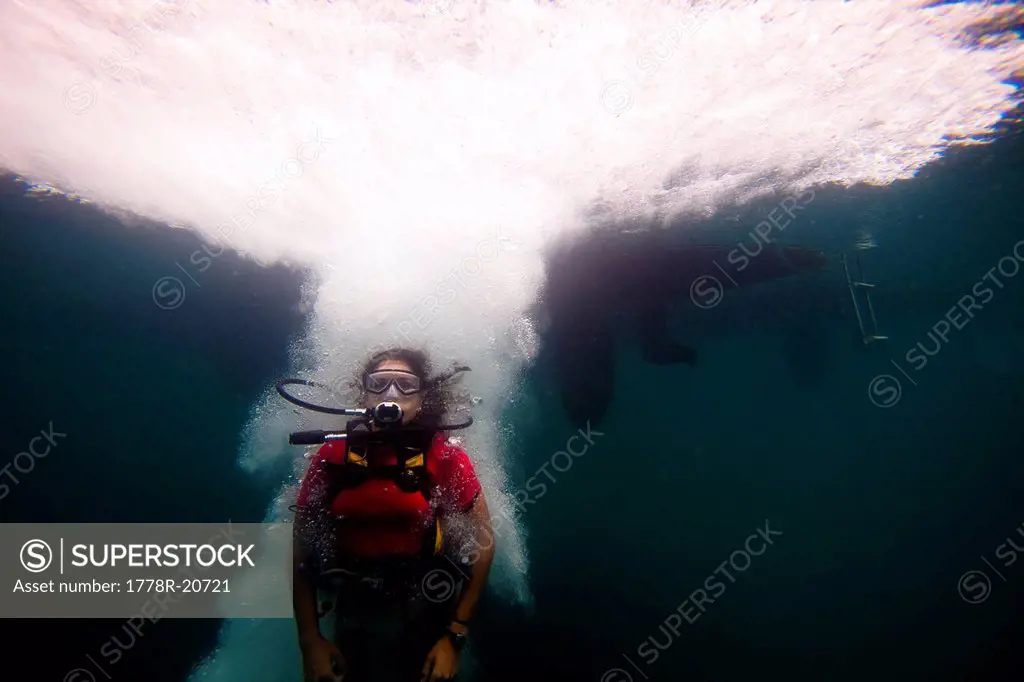 A young Hispanic woman in scuba gear jumps into the ocean.
