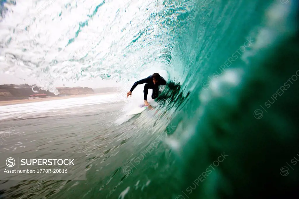 A male surfer pulls into a barrel while surfing at Zuma beach in Malibu, California.