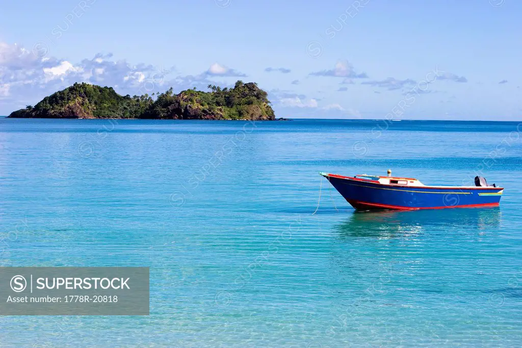 A blue wooden fishing boat floats in the calm waters of Malakati, Fiji.