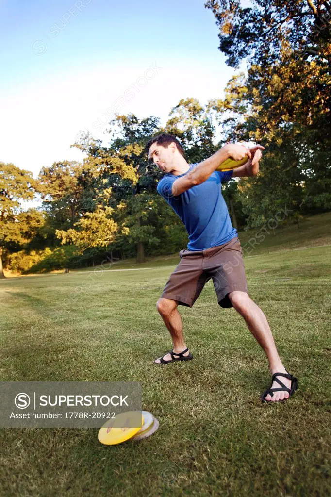 A man makes a backhanded throw playing disc golf.