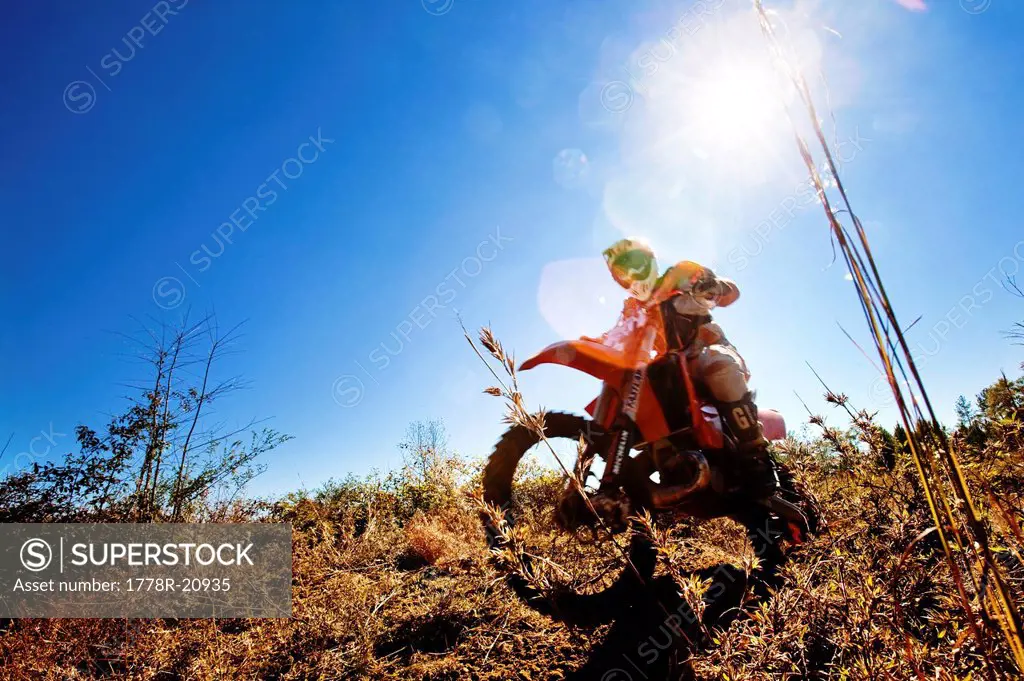 A motorcyclist rides through the brush in an Enduro race in Maplesville, Alabama. Back lit, Lens Flare, Motion Blur