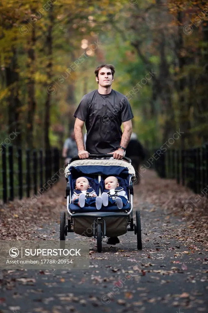 A man runs on a greenway with his two twin sons in a stroller.