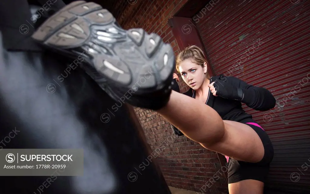 A teenage girl high kicks a punching bag while training for mixed martial arts outside a warehouse in Birmingham, Alabama.