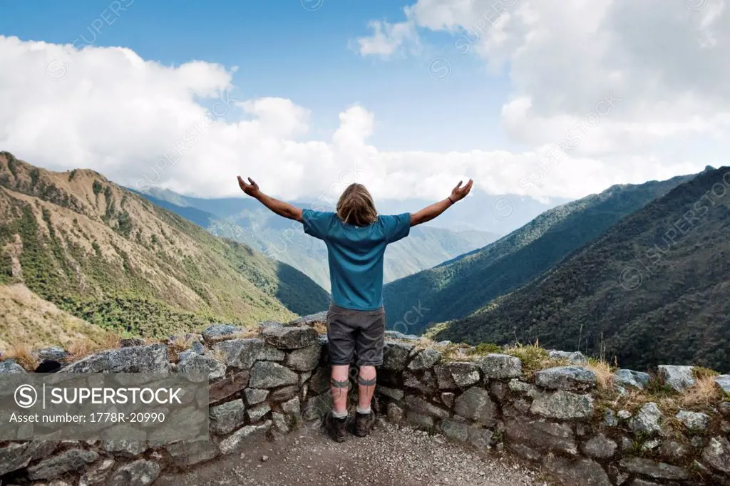 A young man spreads his arms to take in the scenery in the Andes mountains along the Inca Trail.