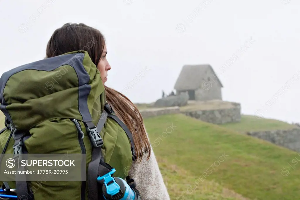 A young woman hikes toward the ancient ruins of Machu Picchu on a foggy morning.