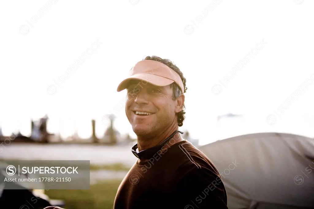 A man in an orange visor with sunglasses softly smiles at the camera.