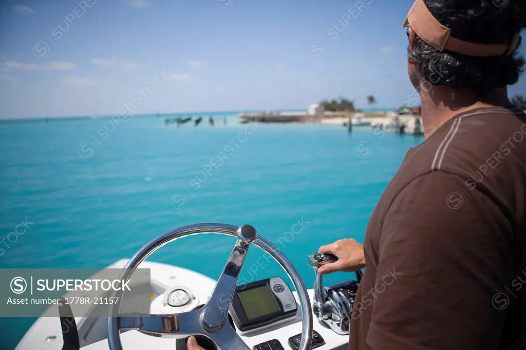 A fisherman steers his boat and hits the throttle from the fly bridge as he gazes out at the blue_green tropical waters.