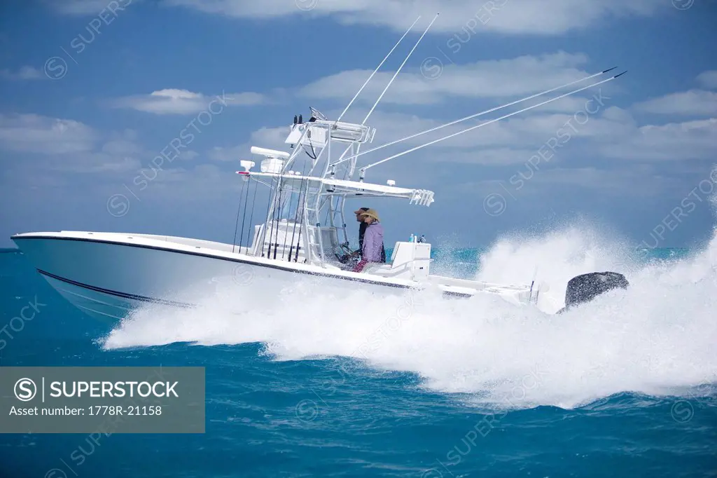 A fishing boat speeds through the blue surf spraying white water.
