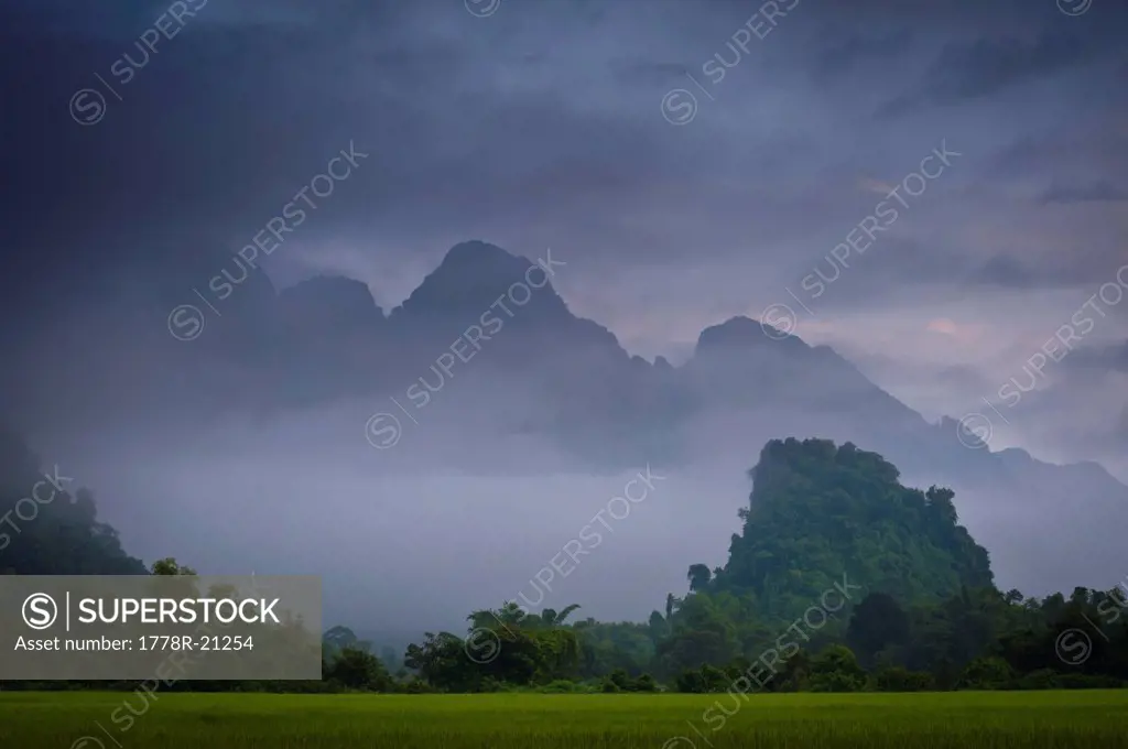 Rice paddies and mountains covered in vegetation in mist and clouds. Vang Vieng, Laos, Asia.