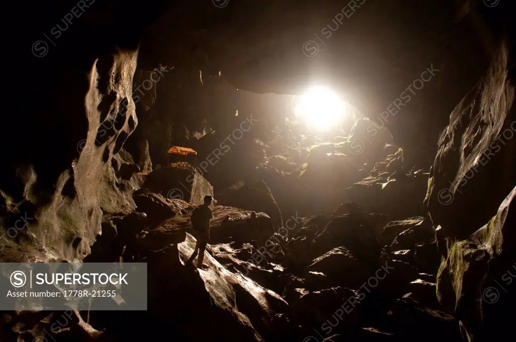 A traveler looking towards the light at the opening of a cave. Vang Vieng, Laos, Asia.
