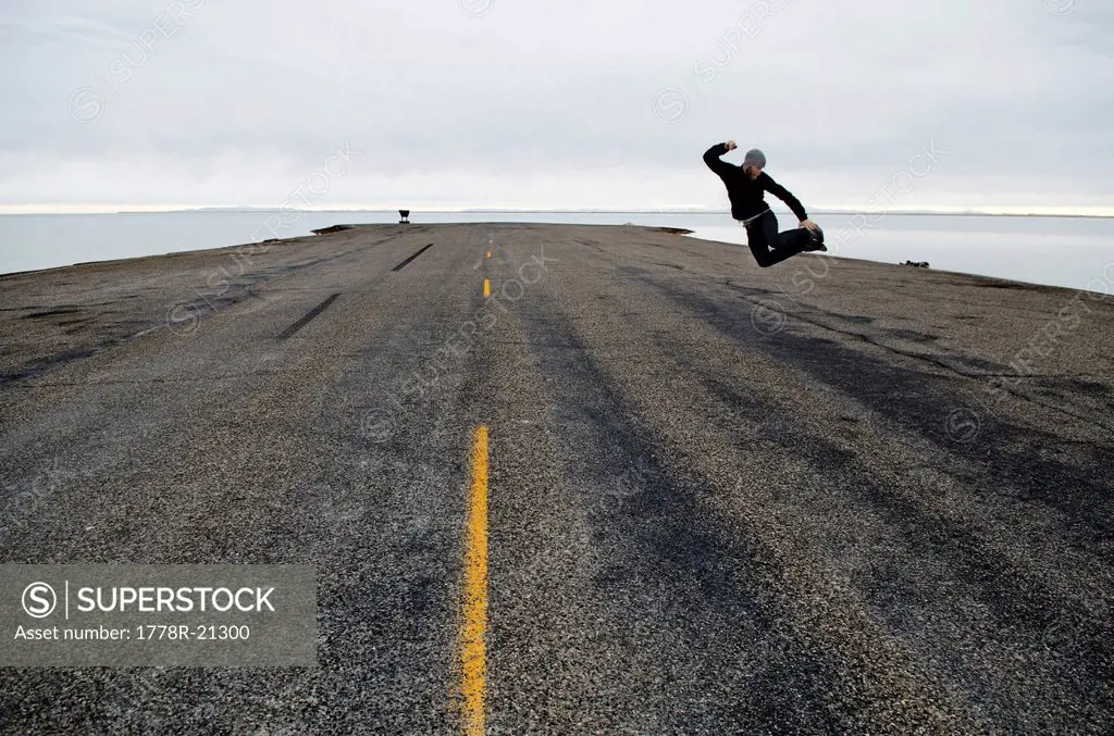 A man jumps in the air at the end of the road and the start of the Bonneville Salt Flats, Utah.