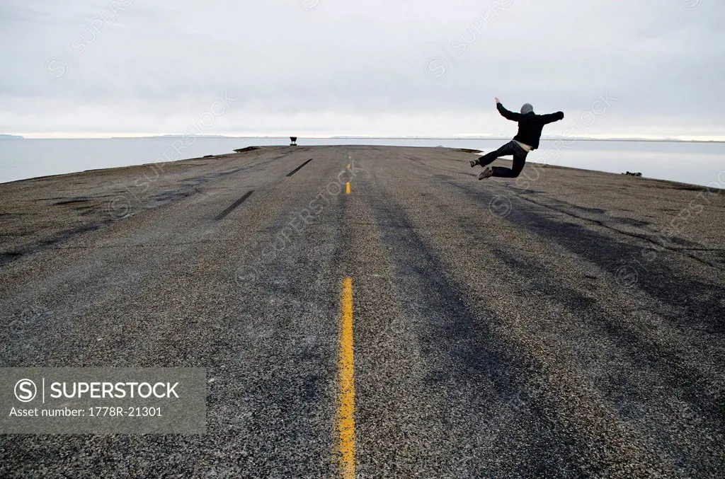A man jumps in the air at the end of the road and the start of the Bonneville Salt Flats, Utah.