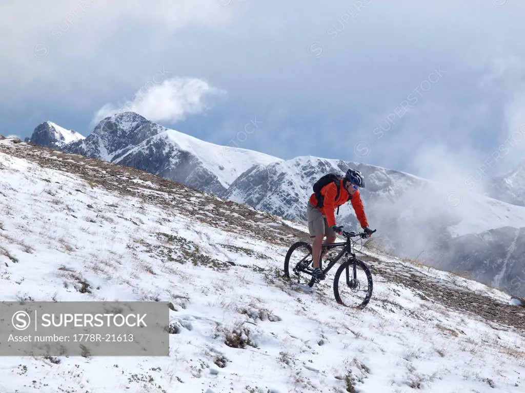 A mountain biker rides through the snow at Kronplatz, mountains and clouds in the background.