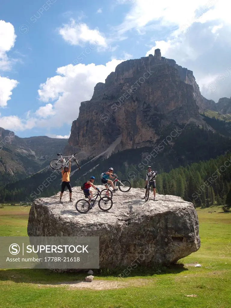 Four mountain bikers are standing with their bikes on a big boulder in a mountain meadow in the Italian Dolomites.