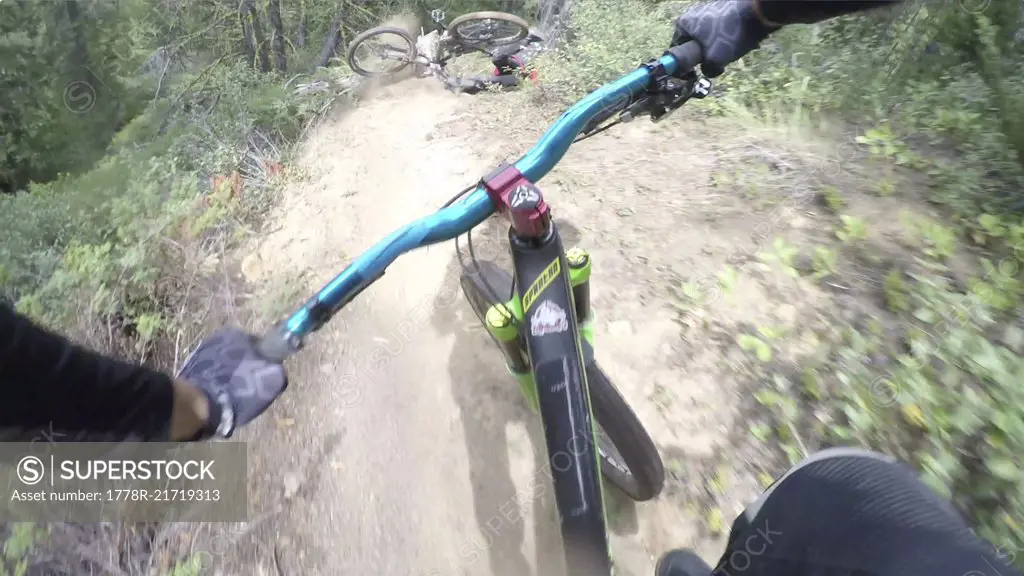 POV past hands of mountain biker on forest ride, friend crashes