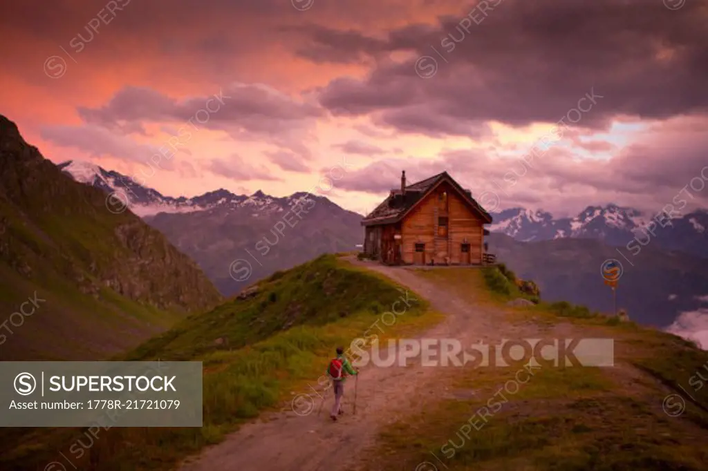A hiker is almost at the Cabane du Mont Fort, a mountain hut near Verbier. The sunset puts the sky in pink and purple colors. It rained all day, and cleared just before this picture. The hut is one of the places hikers stay at during the Haute Route, a classic hike between Chamonix in France and Zermatt in Switzerland.