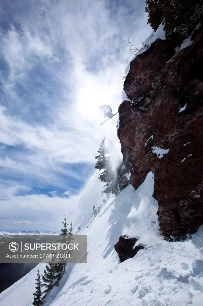 A male skier jumps off a cliff on a sunny day in Colorado.