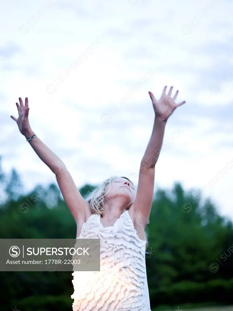 a young girl raises her hands to the sky