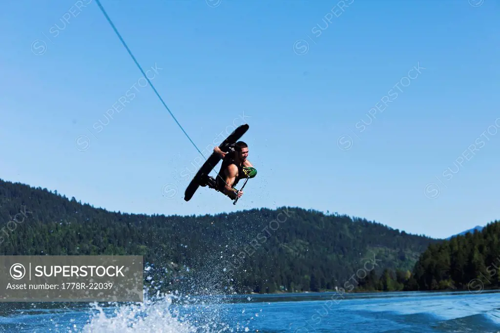 A athletic man wakeboarding jumps huge above the wake and mountains in Idaho.