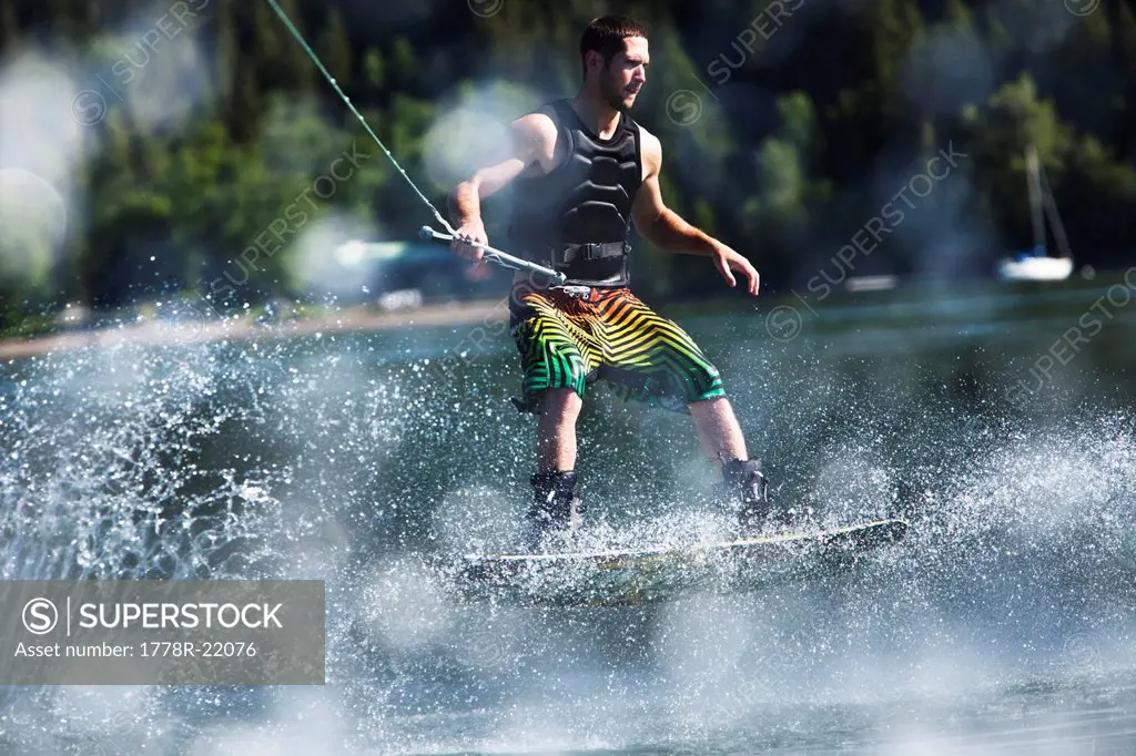 A athletic man wakeboarding pops a huge 180 on a sunny day in Idaho.