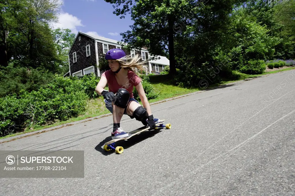 A blonde woman longboards down a New England road.