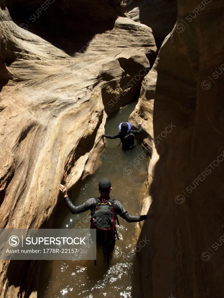 Two people wade through water while hiking down a slot canyon in Utah.