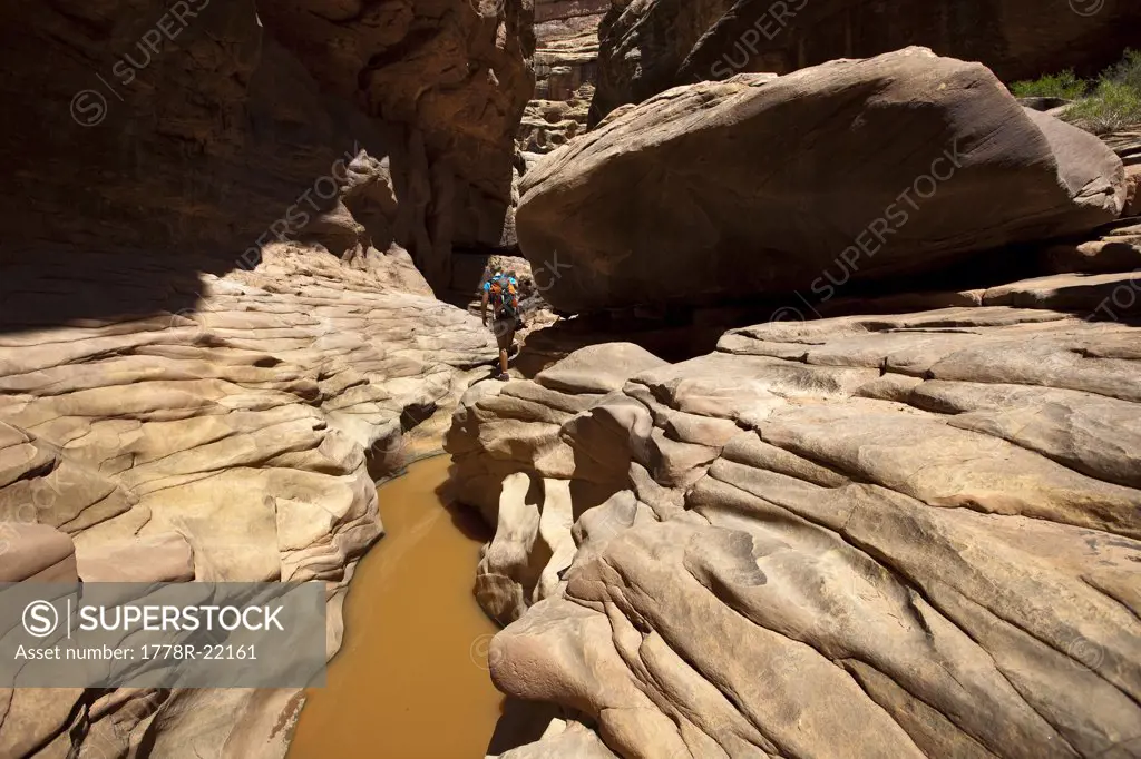 A woman hiking through a canyon with water and interesting rock formations in Utah.