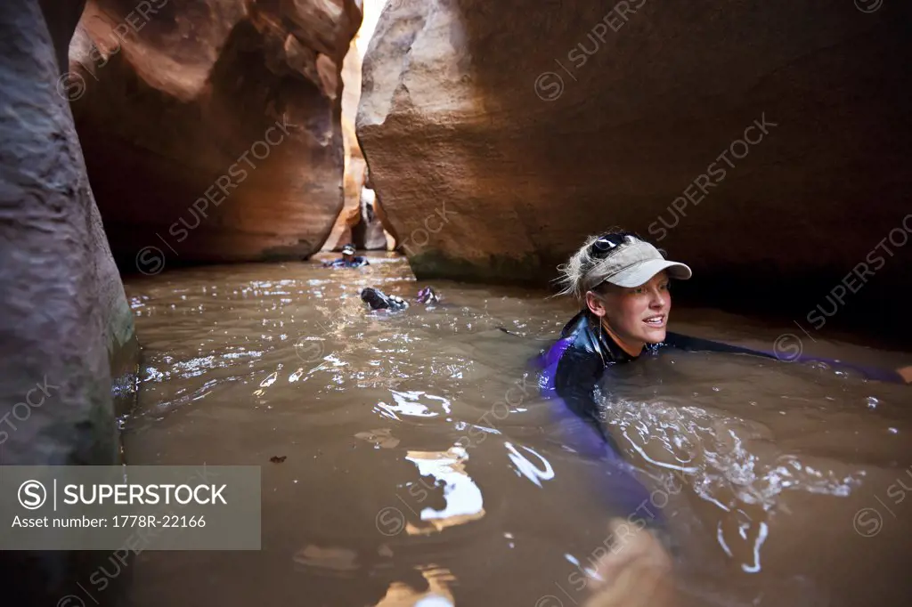 A woman swims through a winding corridor filled with water in a slot canyon in Utah.