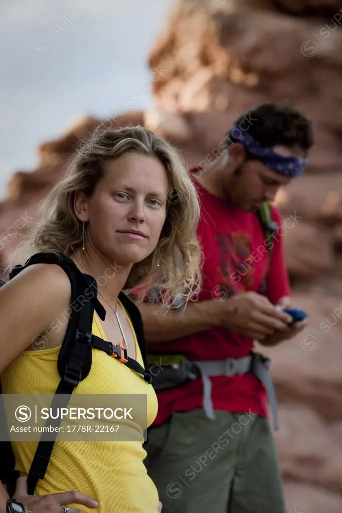 A woman looks at the camera while a man in the background studies his GPS.