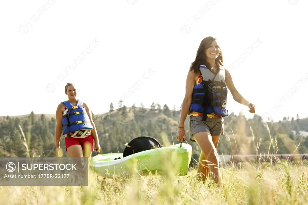 Two girls in life jackets carry a green kayak through a field after a day of kayaking the Yellowstone River in Eastern Montana.