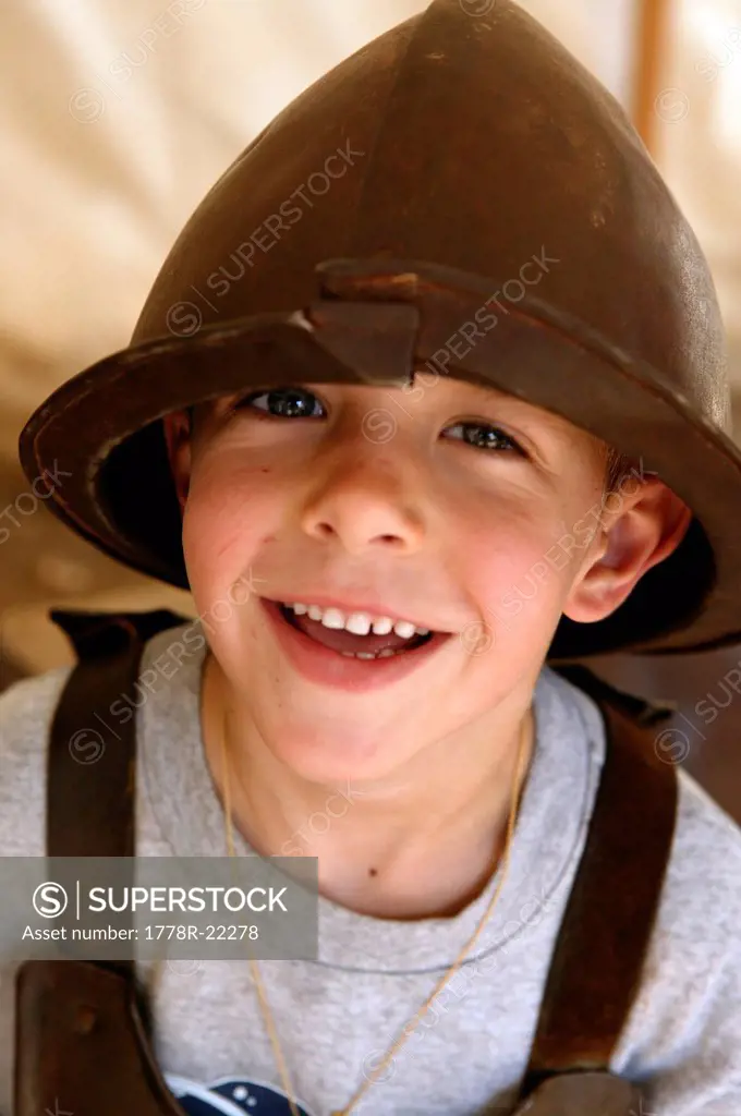 A little boy poses in an old metal helmet.