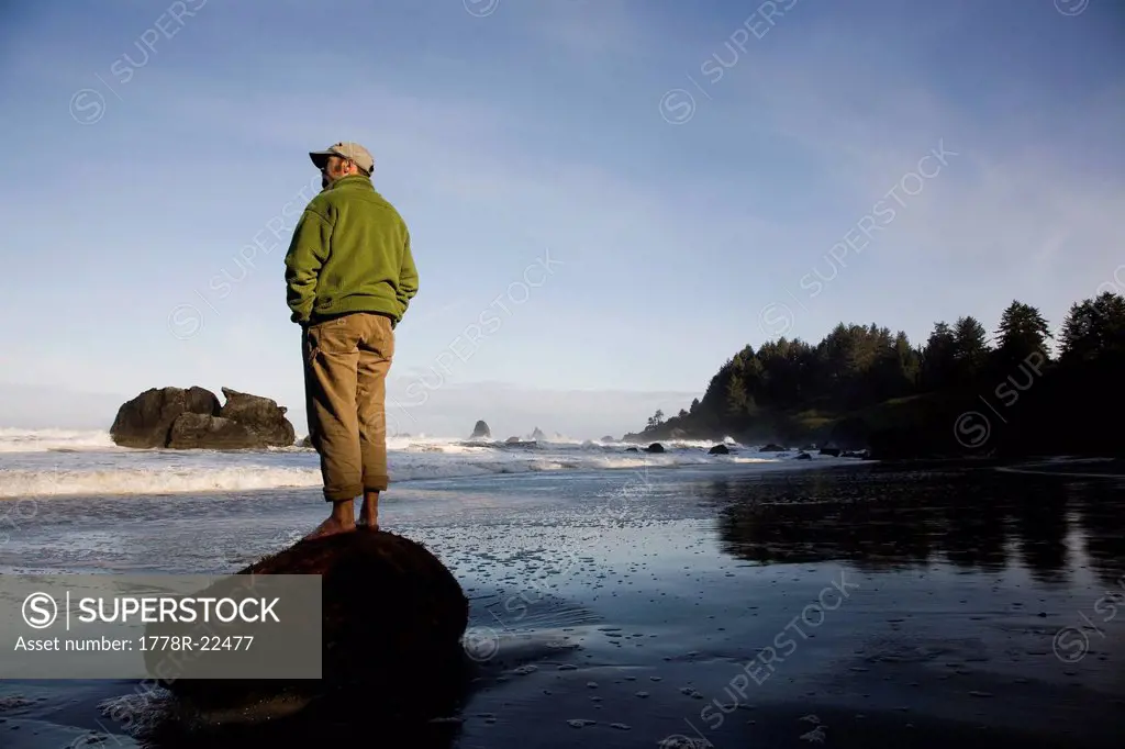 REDWOODS NATIONAL PARK, CALIFORNIA. A man stands alone on a piece of wood on the beach near Redwood National Park.